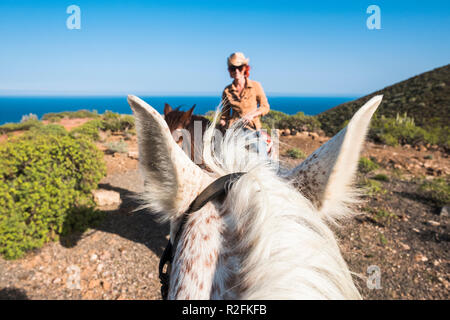 Schöne seltene Portrait von einem schönen Mädchen reiten ein Pferd von einem anderen Reiter auf einem weißen Pferd. lustig und savage Bild für ein Paar, das in Kontakt mit der Natur und einem anderen Lebensstil Stockfoto