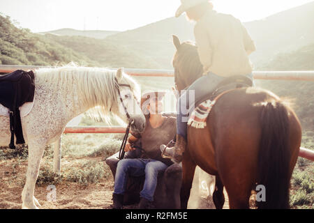 Landschaft und horse farm täglich Szene mit Sonne und Hintergrundbeleuchtung. zwei Pferde und zwei Reiter Mann und Frau Lächeln für einen schönen Tag in der Natur. Freundschaft und tiergestützte Therapie mit Cowboy lifestyle Moderne Stockfoto