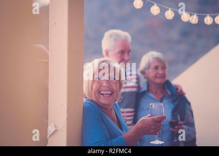 Großes Lächeln für gealterte Frau während der Freizeitaktivitäten auf der Terrasse bei Nacht. Trinken Wein und Spaß an der Party mit Freunden Senior Stockfoto