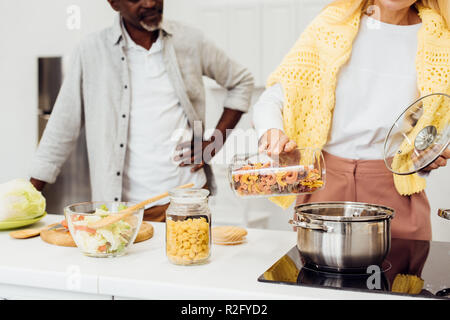 7/8-Ansicht der Frau, die in der Nähe von African American man und kochen Pasta Stockfoto