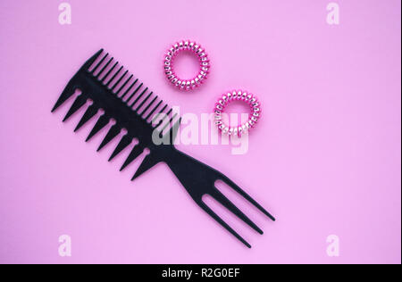 Kunststoff schwarz Kamm und zwei rosa glänzenden scrunchies auf Pastell rosa Hintergrund. Stockfoto