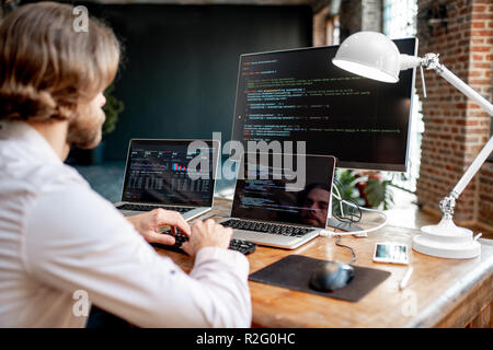 Junge männliche Programmierer ein Programm zu schreiben Code am Arbeitsplatz sitzen mit drei Monitoren im Büro. Bild auf dem Bildschirm Stockfoto