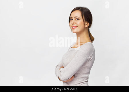 Junge zuversichtlich brünette Frau mit verschränkten Armen lächelt Portrait vor weißem Hintergrund Stockfoto