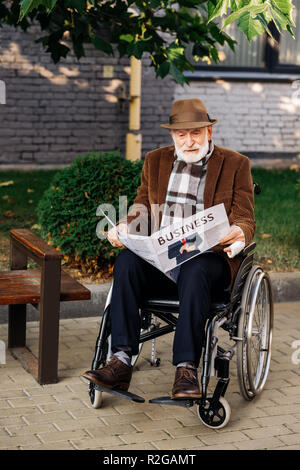 Schöne ältere behinderte Menschen im Rollstuhl lesen Zeitung auf der Straße Stockfoto