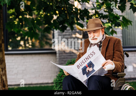 Ältere behinderte Menschen im Rollstuhl lesen Zeitung auf der Straße Stockfoto