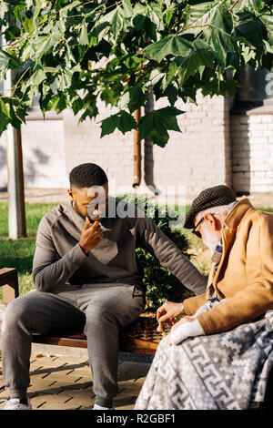 Ältere Menschen und junge afrikanische amerikanische cuidador Schach spielen zusammen auf der Straße Stockfoto