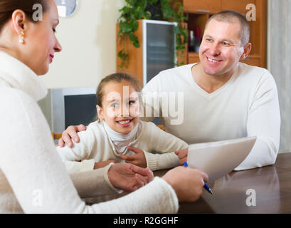 Eltern und kleine Tochter beantworten Fragen von Übertreffenarbeiter im Wohnzimmer zu Hause. Stockfoto