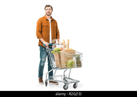 Fröhlicher Mann, der Einkaufswagen mit den Produkten in Papiertüten isoliert auf weißem Stockfoto