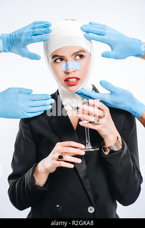 Hände in Handschuhen berühren Frau mit Bandagen nach plastische Chirurgie und Cocktail isoliert auf weißem Stockfoto