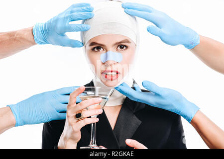 Hände in Handschuhen berühren Frau mit Bandagen nach plastische Chirurgie und Cocktail isoliert auf weißem Stockfoto