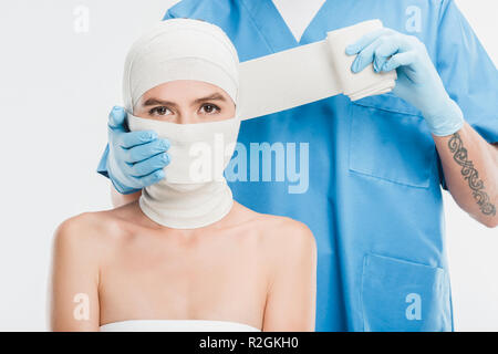 Nahaufnahme der plastischen Chirurgen in Handschuhen bis taping Frau Gesicht mit Bandage isoliert auf weißem Stockfoto