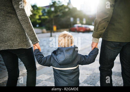 Eine Ansicht der Rückseite kleine Kleinkind Junge mit unkenntlich Eltern gehen im Freien in der Stadt. Stockfoto