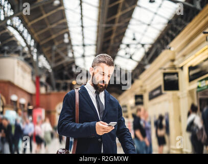 Geschäftsmann mit Smartphone auf dem trian Bahnhof in London, Simsen. Stockfoto