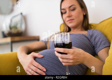 Betroffene schwangere Frau trinkt Rotwein zu Hause Stockfoto