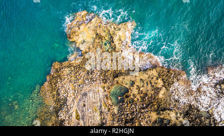 Antenne drone Ausblick auf das Meer und die Wellen, die auf Felsen. ein Mann, der allein Schwimmen in einem natürlichen Pool. Stockfoto