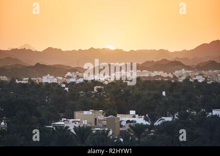 Stadt gegen Bergkette an der idyllischen Sonnenuntergang. Nizwa im Sultanat von Oman. Stockfoto