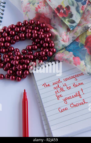 Coco Chanel Zitate auf einen Block Notiz geschrieben, pearl Zubehör und und seidig Blume Shirt, Inspiration phrase" Die mutigen Akt ist noch mit Thi Stockfoto
