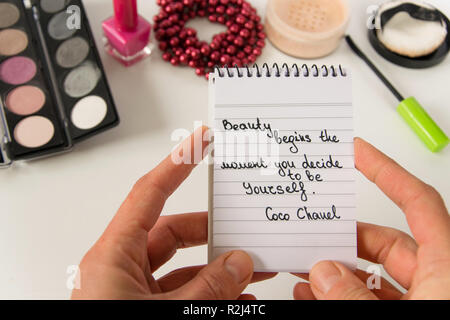 Frau Hand hält Coco Chanel Zitate auf einen Block Notiz geschrieben, pearl Zubehör und bis auf weißem Hintergrund machen, inspiration Satz "Schönheit beginnt die Stockfoto