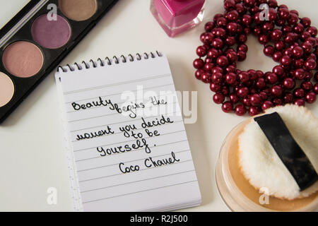 Coco Chanel Zitate auf einen Block Notiz geschrieben, pearl Zubehör und bis auf weißem Hintergrund machen, inspiration Satz "Schönheit beginnt in dem Moment, in dem Sie entscheiden Stockfoto