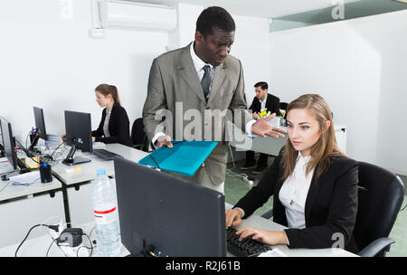 Zornigen Mann Chef pointinting zu vermisst in der Arbeit zu weiblicher Manager am Laptop arbeiten Stockfoto