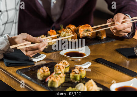 7/8-Ansicht von Menschen essen Sushi mit Stäbchen im Restaurant Stockfoto