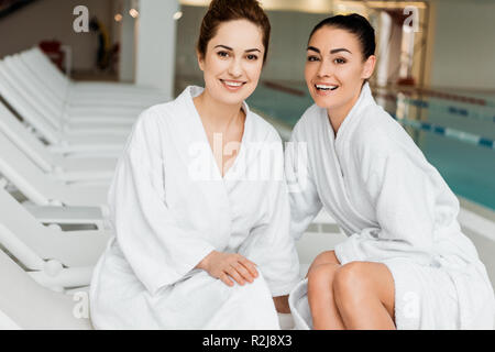 Glückliche junge Frauen in bademänteln an Kamera Lächeln beim zusammen Entspannen im Spa Stockfoto