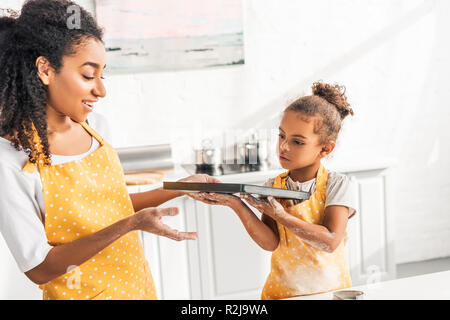 Afrikanische amerikanische Mutter und Tochter holding Fach mit Ungebackene Kekse in der Küche Stockfoto