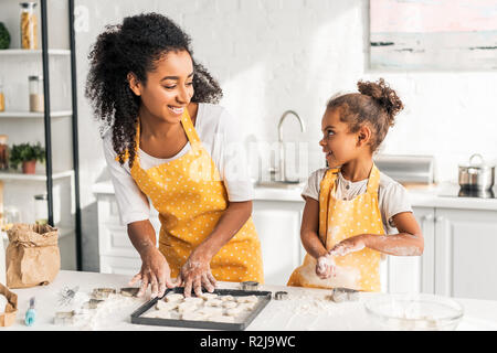 Lächelnd afrikanischen amerikanischen Mutter und Tochter Vorbereitung cookies und an jedem anderen Suchen in der Küche Stockfoto