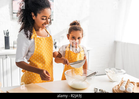 Gerne afrikanische amerikanische Mutter und Tochter Zubereitung Teig und Sieben Mehl zusammen in der Küche Stockfoto