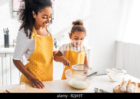Fröhlich afrikanische amerikanische Mutter und Tochter Teig vorbereiten und Sieben Mehl in der Küche Stockfoto