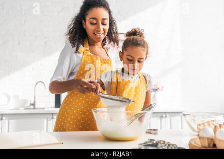 Afrikanische amerikanische Mutter, Tochter Teig vorbereiten und Sieben Mehl in der Küche Stockfoto