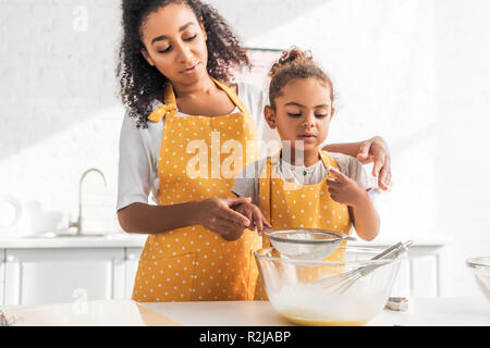 Afrikanische amerikanische Mutter und Tochter Zubereitung Teig und Sieben Mehl zusammen in der Küche Stockfoto