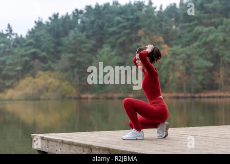 Frau gekleidet in Sportkleidung binden ihr Haar, bevor sie draußen läuft an einem See Stockfoto