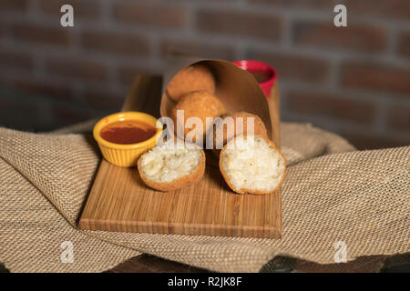 Gebratene Risotto Kugeln mit zwei verschiedenen Soßen auf Holzplatte mit Ziegel Wand Hintergrund Stockfoto