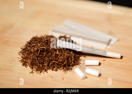 Hand rollen Tabak, Papier und Filter Zigaretten auf rustikalem Holz machen Stockfoto