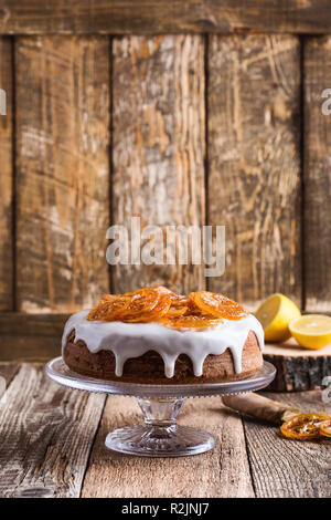 Hausgemachte Kuchen von Zitrusfrüchten mit Zitrone Glasur und kandierten Früchten Slices auf Kuchen stehen auf rustikalen Holztisch Stockfoto