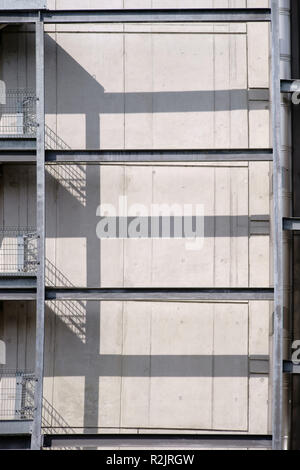 Ein Geländer aus Stahl mit einer externen Treppe wirft symmetrische Schatten gegen eine Betonwand Stockfoto