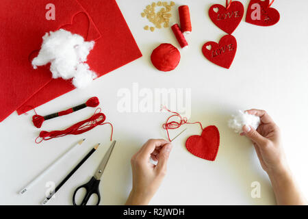 Valentinstag Filz Kunsthandwerk. Frau Hände nähen roten Herzen. DIY. Flach. Ansicht von oben Stockfoto