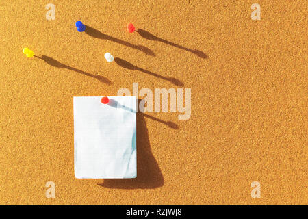 Orange Cork board mit einem Papier Hinweis befestigt und mehrere andere Farbe Pins oben mit Schatten von der Seite Sonnenlicht durch die Fenster leeren Raum Stockfoto