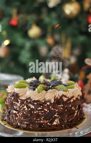 Schokolade Obstkuchen mit Kiwi, Pflaumen und geschlagener Sahne und Schokolade Stück um mit Weihnachtsschmuck Stockfoto