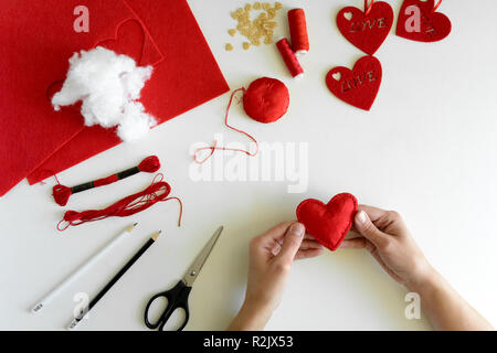 Valentinstag Filz Kunsthandwerk. Frau Hände nähen roten Herzen. DIY. Flach. Ansicht von oben Stockfoto