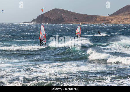 Windsurfer und Kitesurfer in der Bucht von Medano an der Küste von Teneriffa in starken Wind. Im Vordergrund die Brandung vor dem Panorama der Montana Roja. Stockfoto