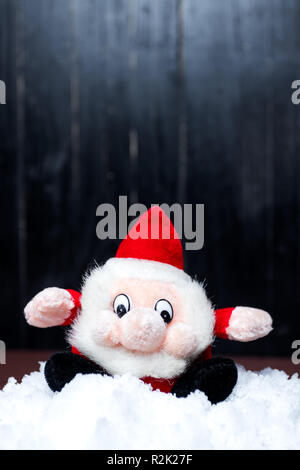 Lustige weihnachten santa claus Rot und Schwarz Maskottchen. Auf dem Schnee. Schwarzen Hintergrund. Vertikale Ausrichtung. Kopieren Platz an der Spitze. Stockfoto