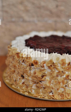 Cherry sauer Haselnuss Cake mit cherry Dressing top und Haselnuss Stücke um mit Schlagsahne auf hölzernen Tisch serviert Stockfoto