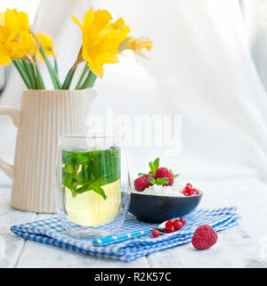 Tee mit Minze im Glas und Müsli zum Frühstück auf den Tisch am Fenster. Gute Frühling Morgen Stockfoto