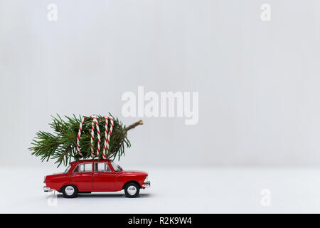 Rote Spielzeugauto mit einem Weihnachtsbaum auf dem Dach, weißer Hintergrund, geringe Tiefenschärfe. Stockfoto