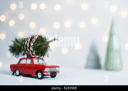 Rote Spielzeugauto mit einem Weihnachtsbaum auf dem Dach, Girlande bokeh auf dem Hintergrund, geringe Tiefenschärfe. Stockfoto