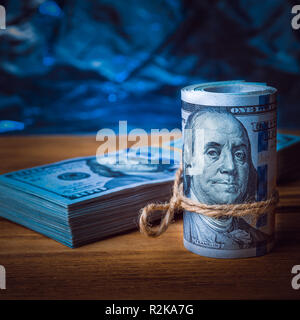 Eine Rolle der Dollar mit einem Pack von Dollar auf dem Hintergrund von texturierten Holzbretter in blaues Licht Stockfoto