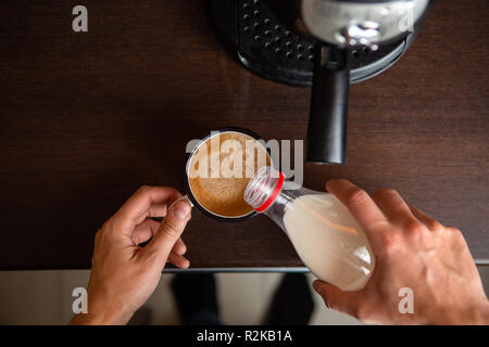 Foto der Kaffeemaschine, die Hände des Menschen gießen Milch in die kaffeetasse Stockfoto