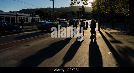 Die Passanten über die quaibrücke in Zürich im Abendlicht werfen lange Schatten Stockfoto